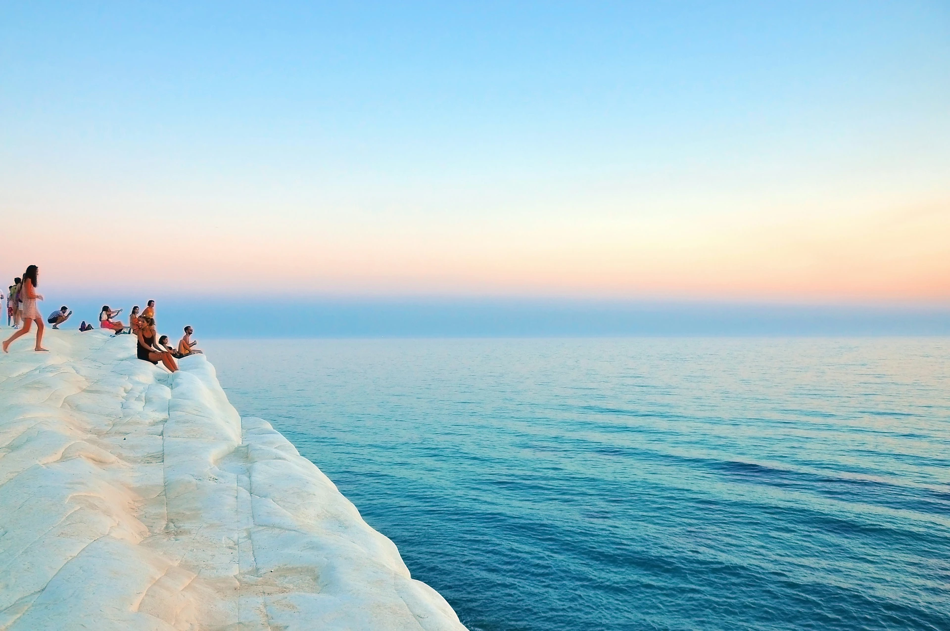 People gathering on coastal rocks beside the sea at sunset